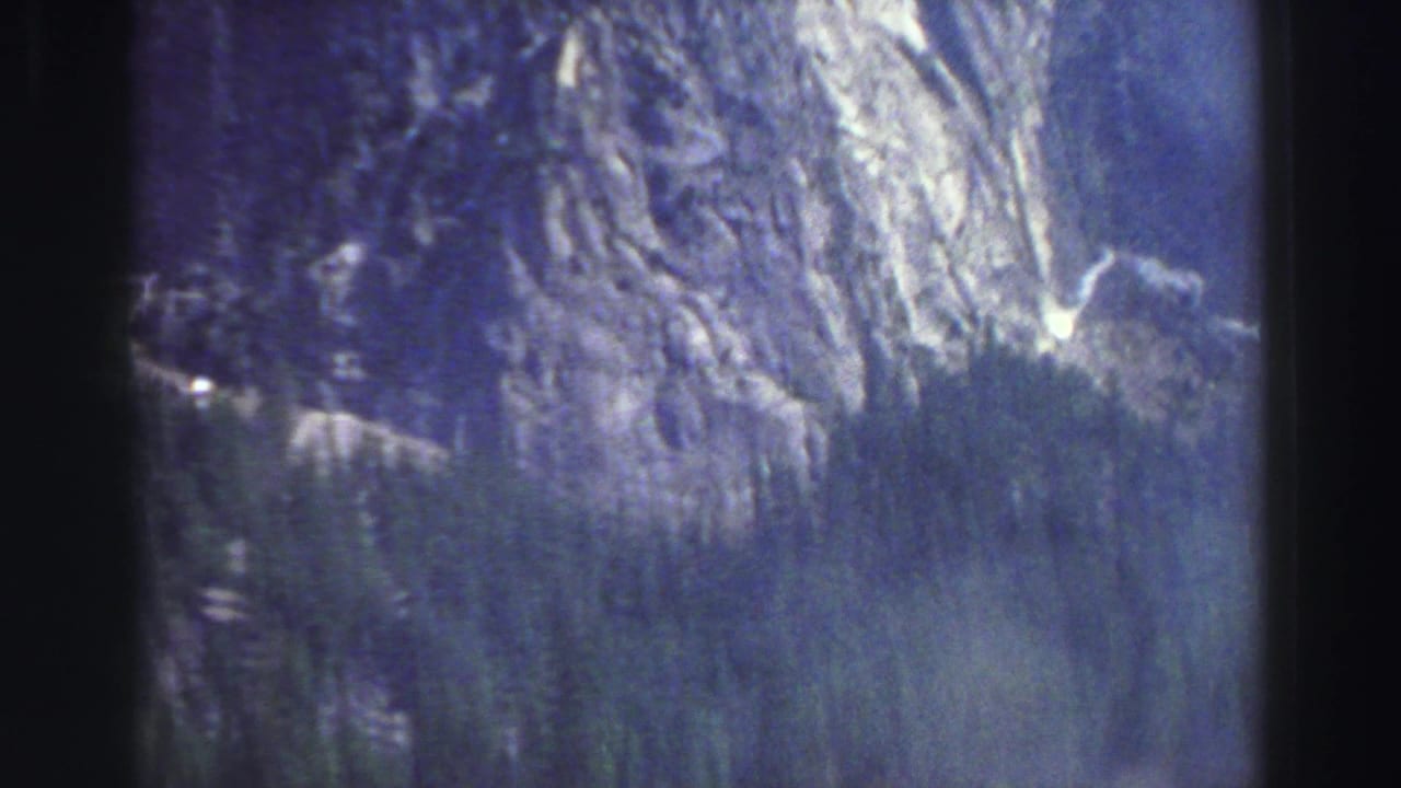 Granite mountain slope and evergreen trees seen through soft blue-purple film color.