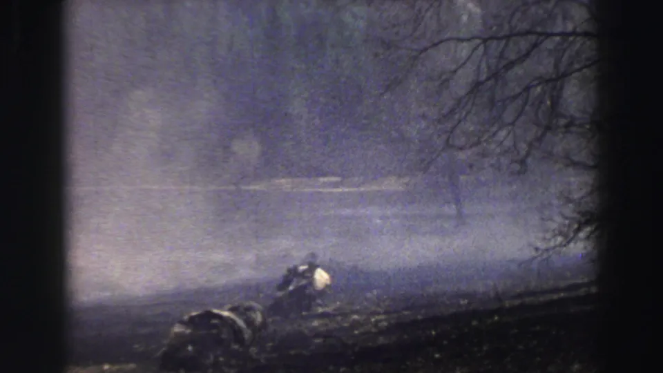 The 8mm frame shows storm haze and dark terrain near Lake Tahoe, with bare branches and a small distant figure or object partly obscured.