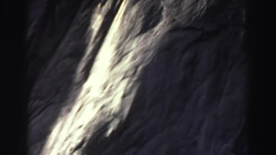 1969 Lake Tahoe 8mm frame showing a closer section of the cliff, with bright glare across rough stone and heavy shadow at the edge.