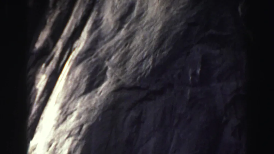 1969 Lake Tahoe 8mm frame showing a textured gray rock wall, a narrow bright sunlit line, and dark shadowed areas from handheld framing.