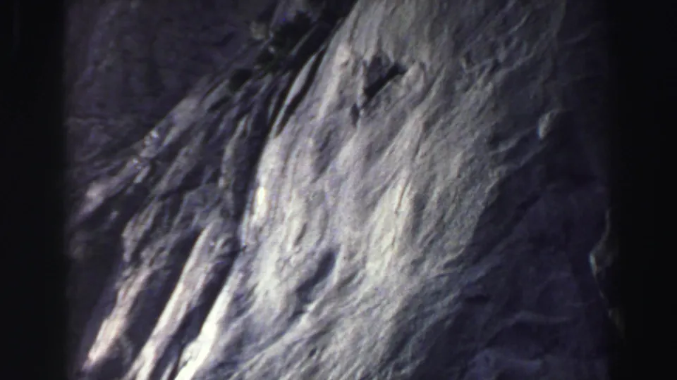 Soft, abstract 8mm frame from the 1969 Lake Tahoe road clip, showing pale textured shapes and gate-edge shadow.