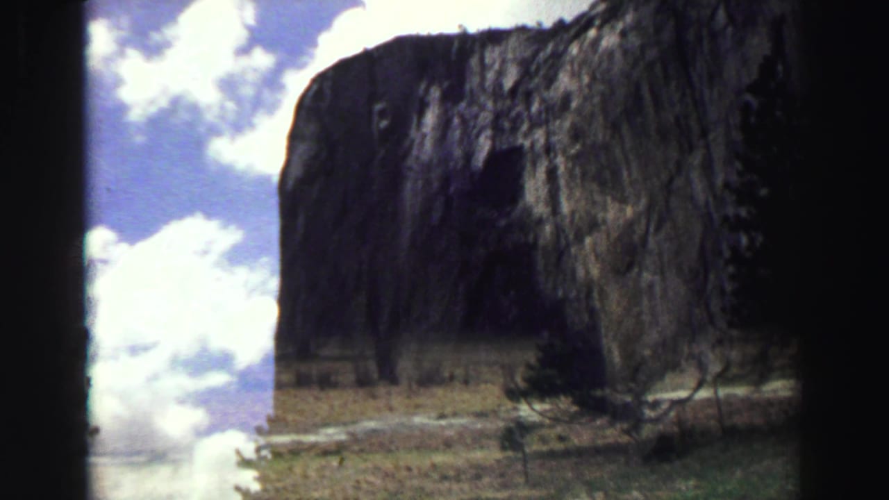 Sheer mountain cliff under bright clouds with dark film borders.