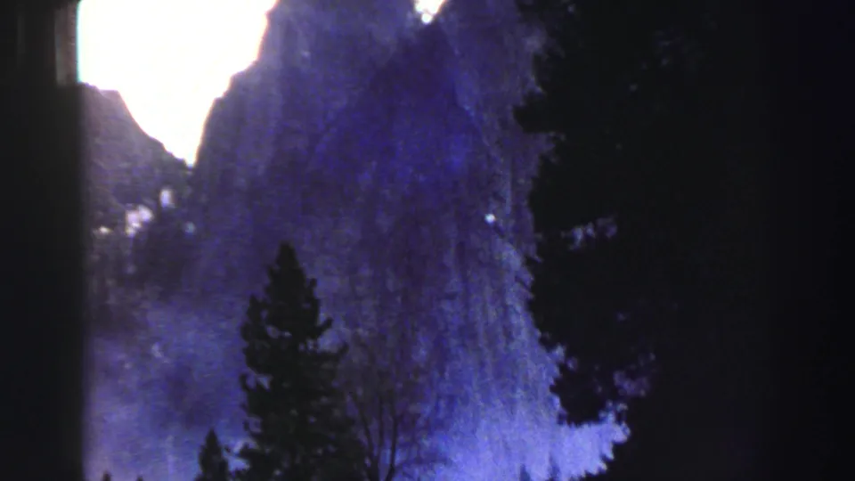 1969 Lake Tahoe 8mm frame showing a waterfall descending along a cliff, with pine trees and shadowed rock in the foreground.