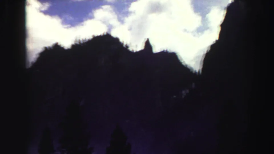 1969 8mm Lake Tahoe-area view of silhouetted mountain peaks beneath a bright cloudy sky.