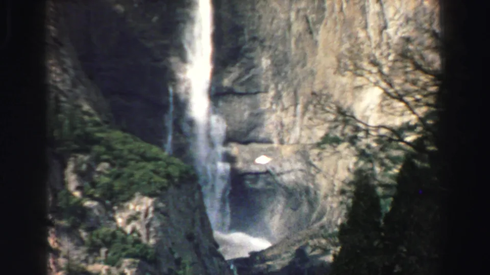 Final Lake Tahoe 8mm frame showing a waterfall descending a rugged cliff, bordered by evergreens and shadowed branches.