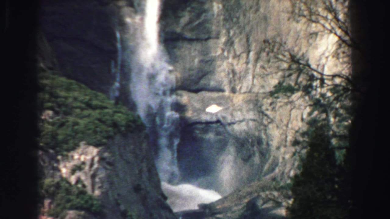 Waterfall and cliff face framed by trees and brush.