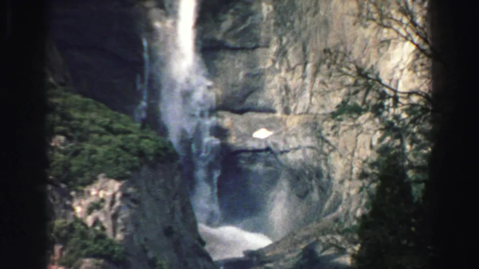 Lake Tahoe waterfall view on 8mm film, with falling water, rock wall, brush, and bare branches in the frame.
