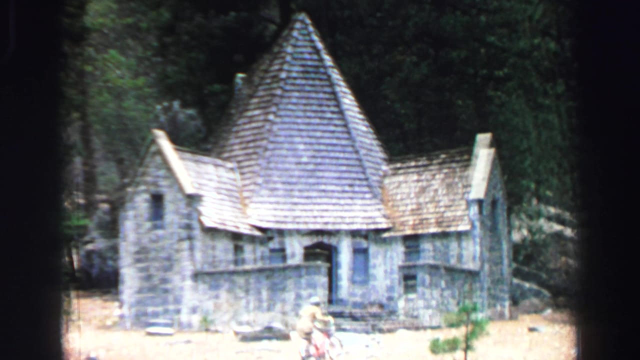 1969 Lake Tahoe 8mm frame showing a rustic stone building with a steep conical roof among trees, with a person near the entrance area.