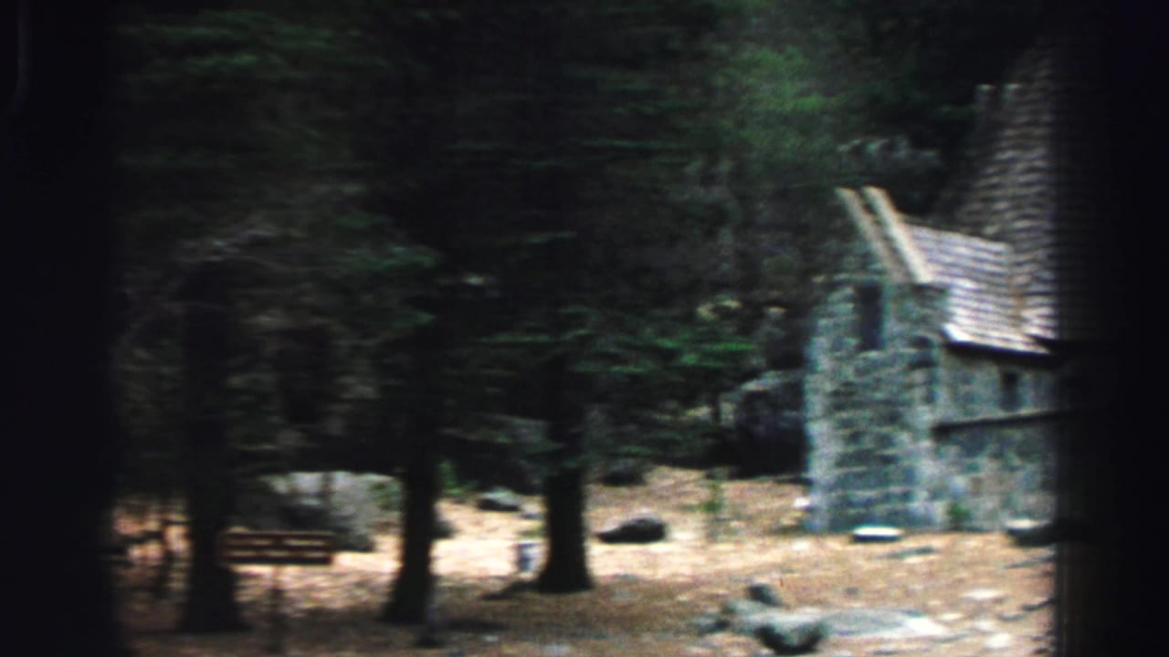 1969 Lake Tahoe home-movie frame showing the stone building partly cropped at right, seen through a shaded stand of trees.