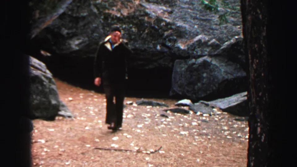 1969 Lake Tahoe home-movie still of a suited man approaching the camera through rocky forest terrain.