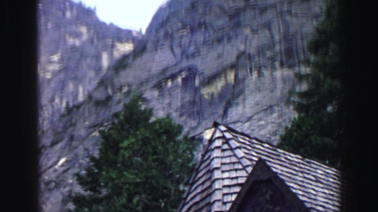 Shingled roof edge and evergreen trees beneath tall granite cliffs.