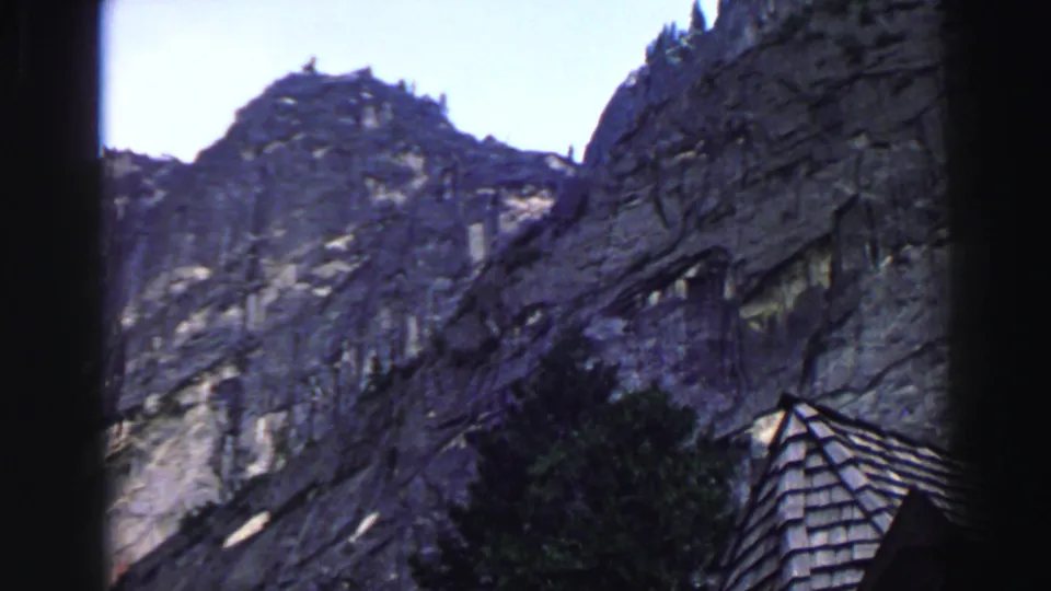 1969 Lake Tahoe 8mm frame emphasizing the granite mountainside, trees, and a small roof corner at the lower edge.