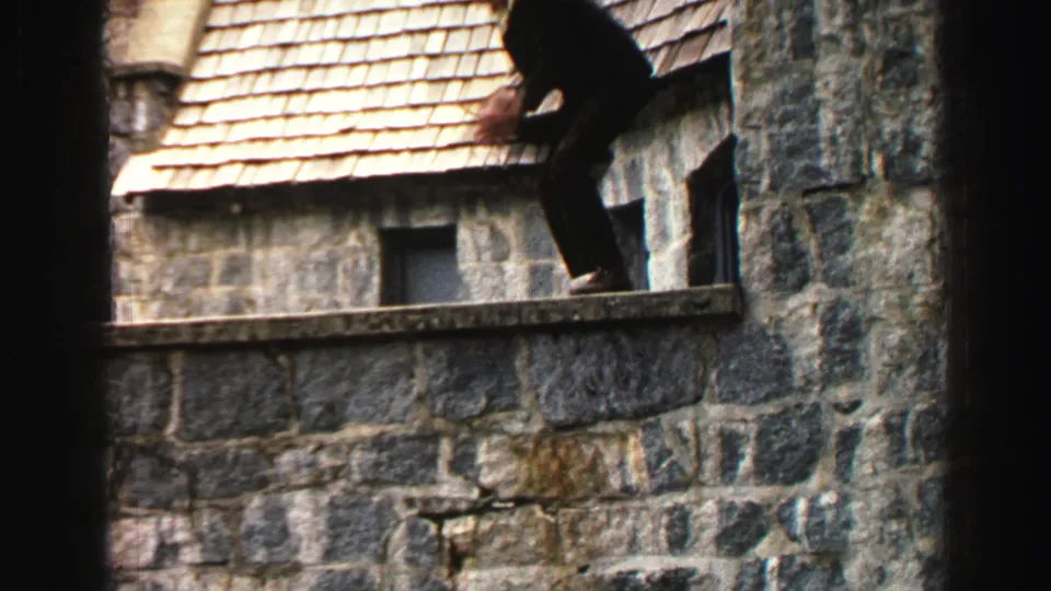 The suited man steps along the high stone ledge at the Lake Tahoe building in a warm 1969 8mm home-movie frame.