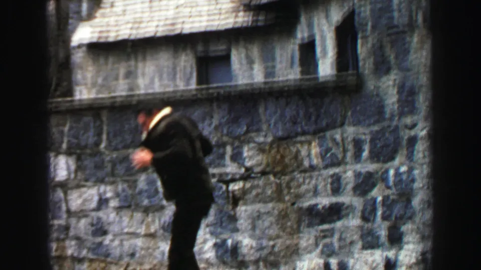 1969 Lake Tahoe frame with motion blur as the man steps down from the ledge beside the rustic stone building.