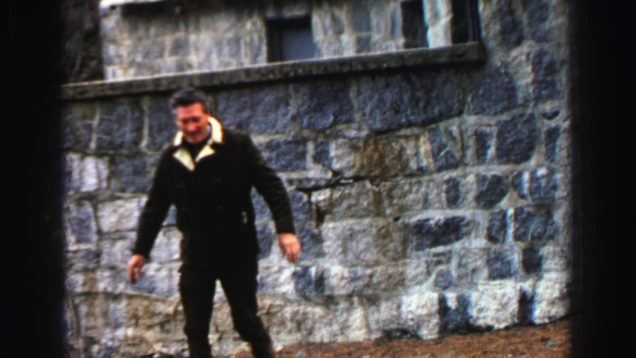 Man in a dark coat walks beside a stone building wall.