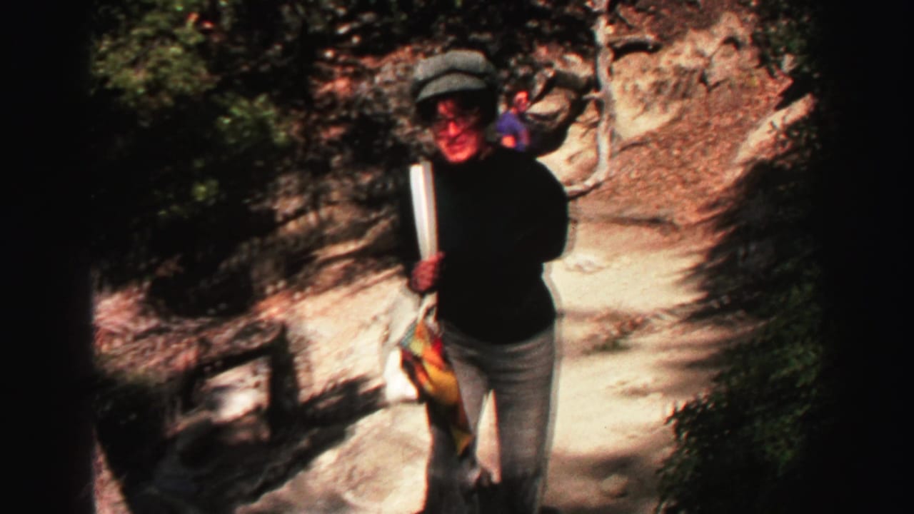 A hiker walks toward the camera on a rocky trail beside sunlit stone and brush.