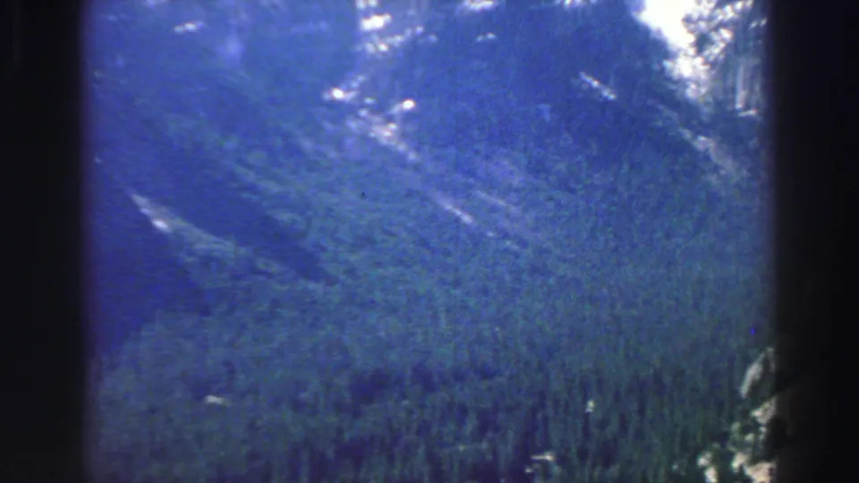 1969 Lake Tahoe scenic frame showing a broad wooded valley below rocky mountain slopes in faded 8mm color.