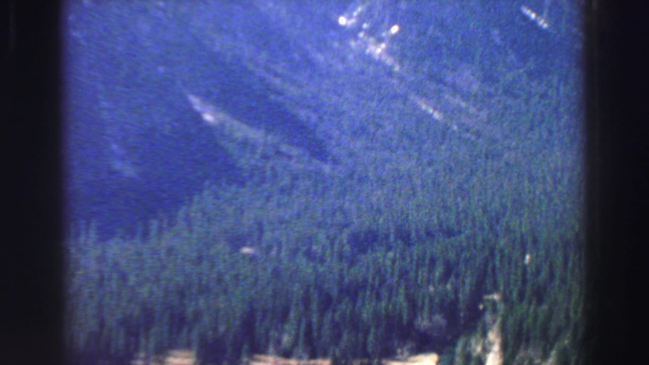 High view over dark evergreen forest and mountain slope with film-frame borders.