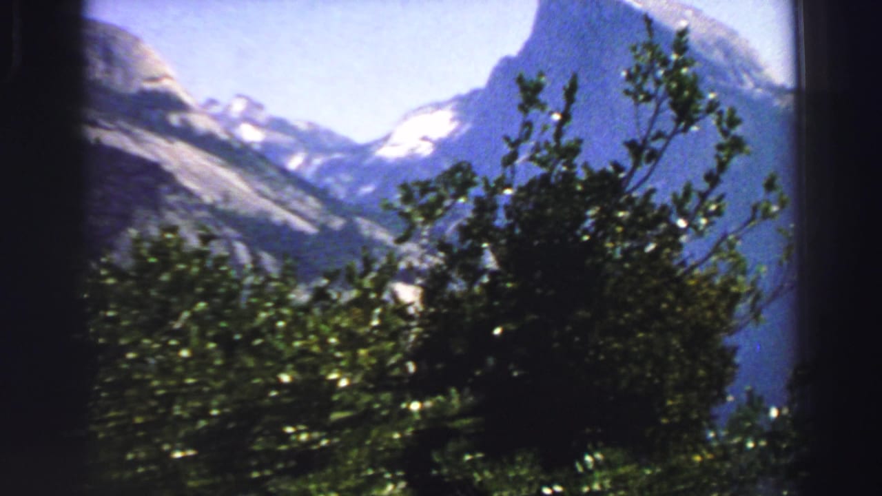 Lake Tahoe-area scenic frame from 1969 with leafy foreground branches, distant mountain ridges, snow patches, and a bright blue sky.