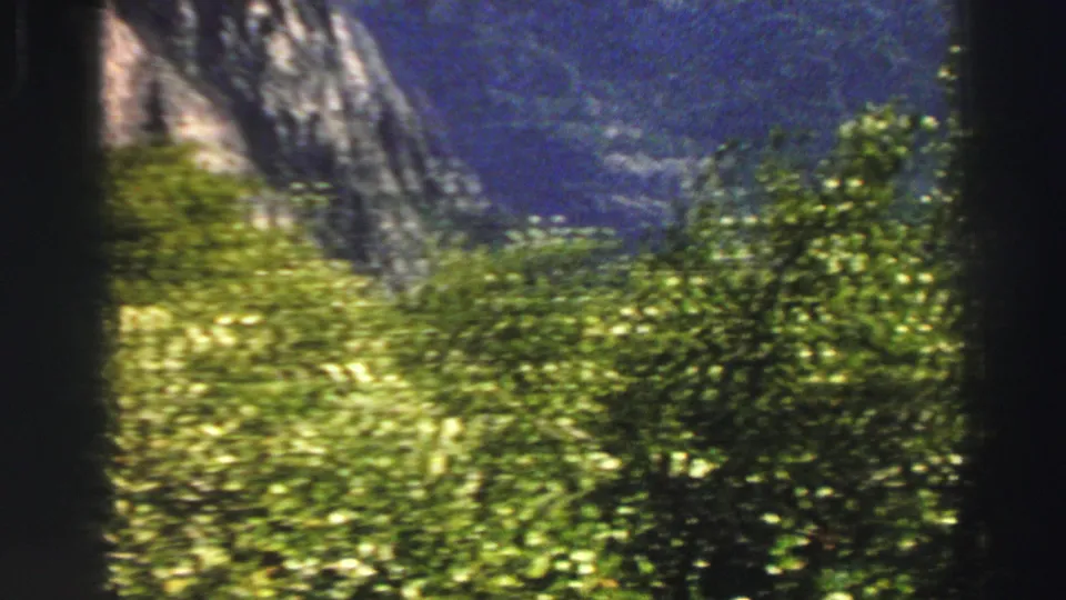 Vintage Lake Tahoe landscape frame with sunlit shrubs, steep mountain walls, and a darker valley beyond.