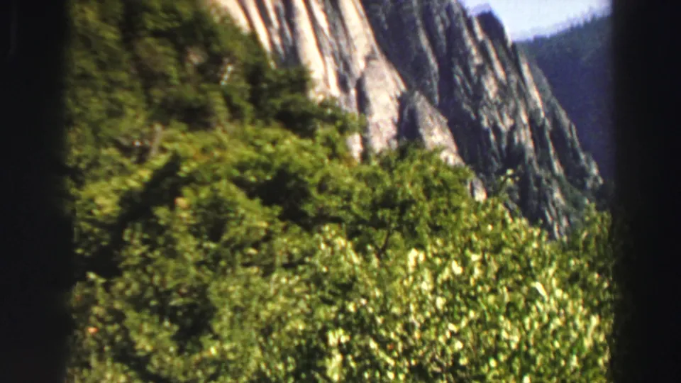 1969 Lake Tahoe 8mm frame showing thick green vegetation against a steep pale mountain rock face.