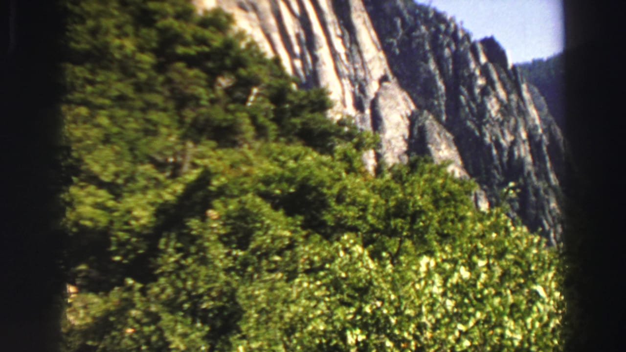 Forested slope and pale rock face seen from a shaded mountain overlook.
