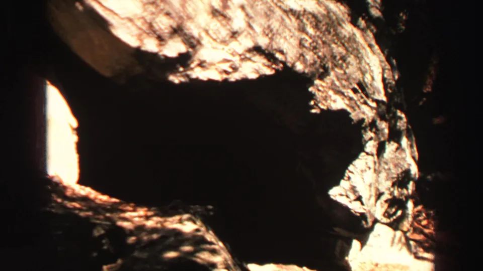 High-contrast 8mm view of a shadowed rocky opening and sunlit granite near the Lake Tahoe mountain landscape.