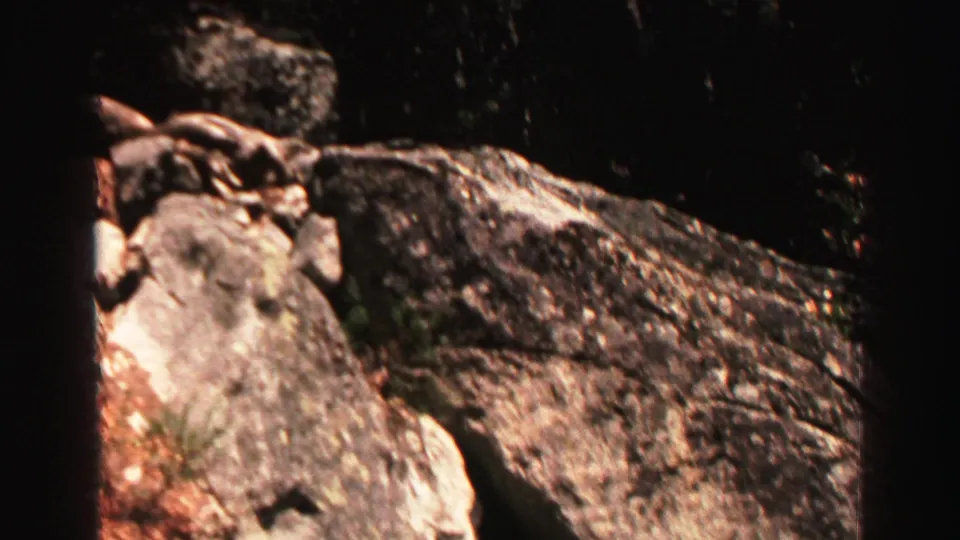 Lake Tahoe area 8mm frame showing rough granite rocks, dark surrounding foliage, and a vertical dark border from the filmed viewpoint.