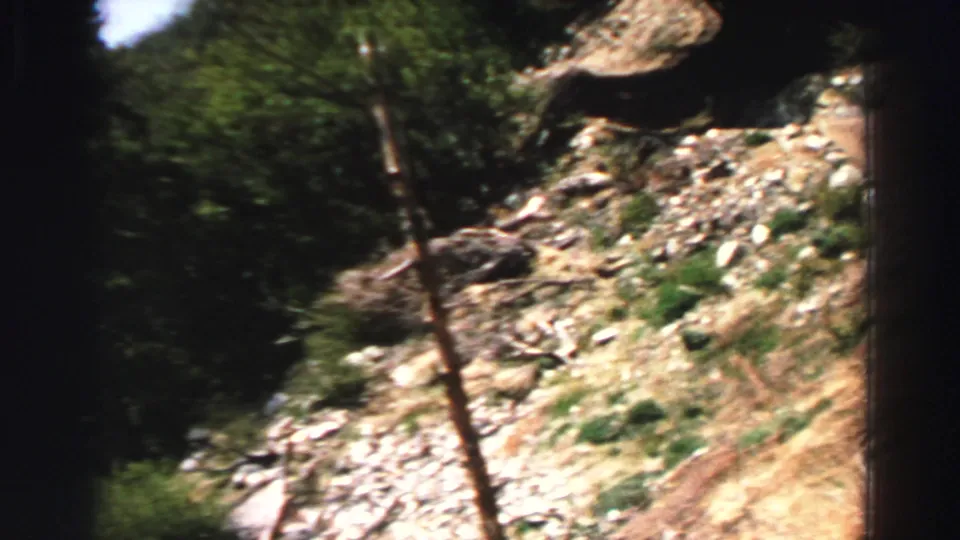 Handheld 8mm view of a narrow dirt trail, rocks, dry grass, and shaded trees on a Lake Tahoe hillside.