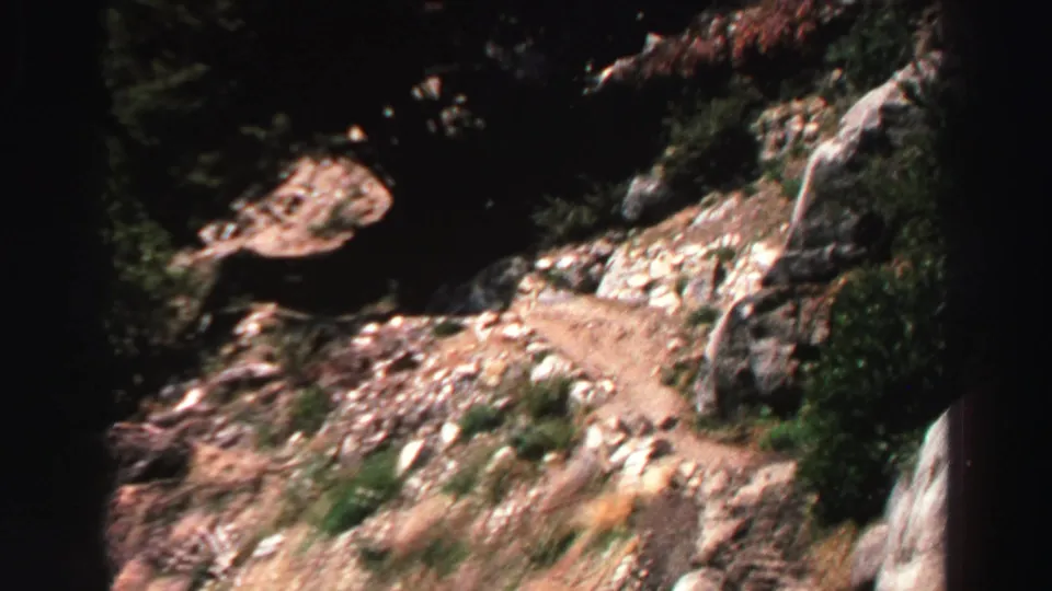 Lake Tahoe 8mm frame with a curving dirt path, boulders, brush, and dark tree shade on rugged mountain terrain.