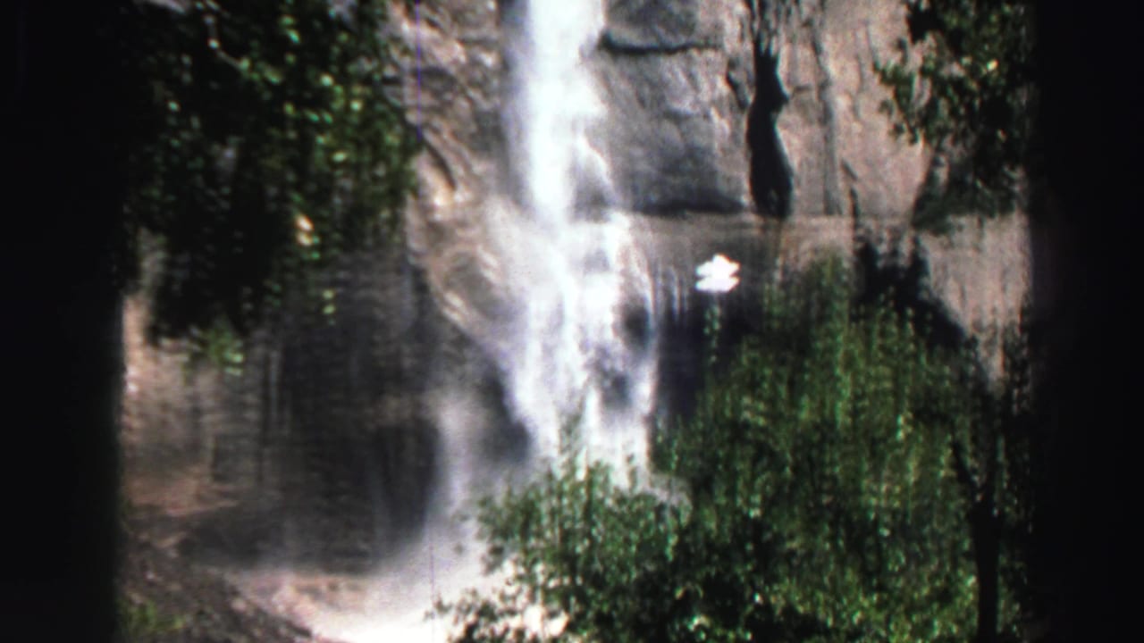 1969 Lake Tahoe 8mm frame with a bright waterfall descending a gray cliff behind green foliage.