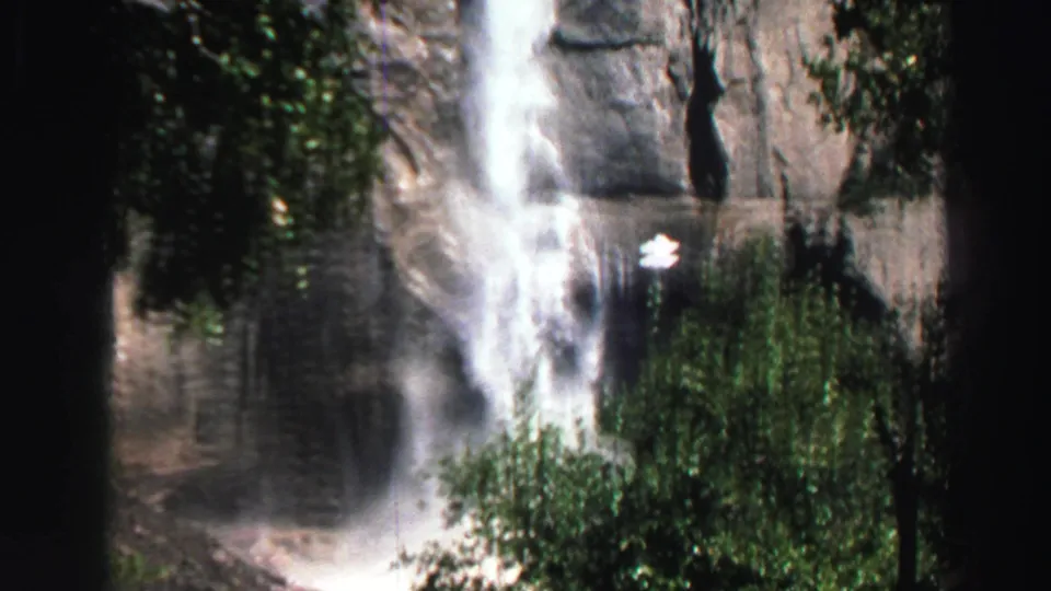 1969 Lake Tahoe 8mm frame with a bright waterfall descending a gray cliff behind green foliage.