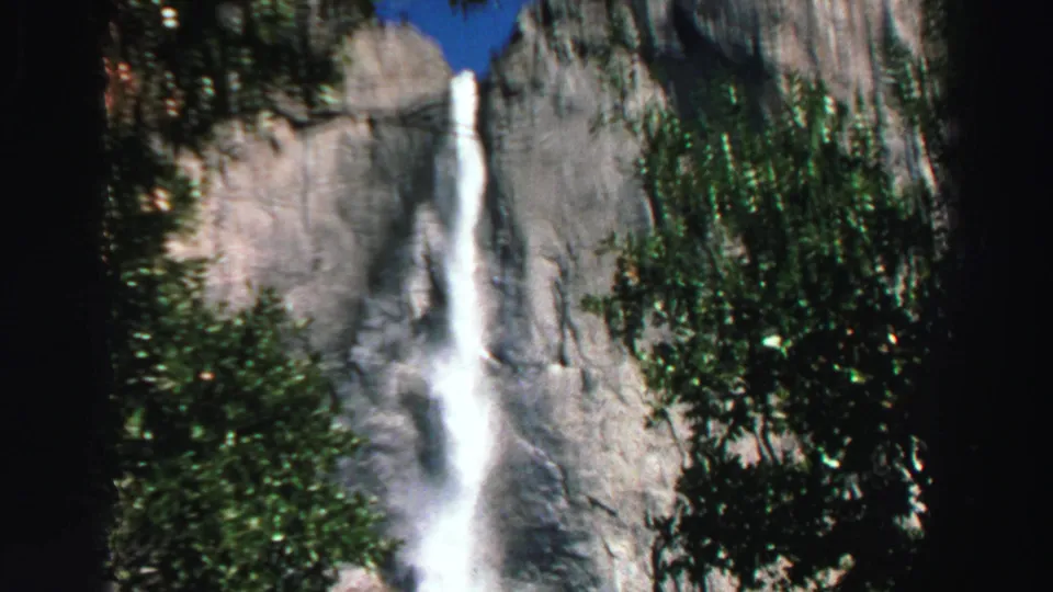 1969 Lake Tahoe frame showing the tall waterfall from a wider angle, framed by trees and a gray cliff.