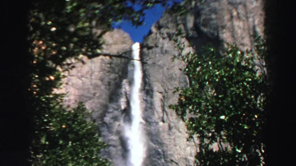1969 Lake Tahoe-area 8mm frame showing a waterfall framed by trees, granite rock, blue sky, and dark film edges.