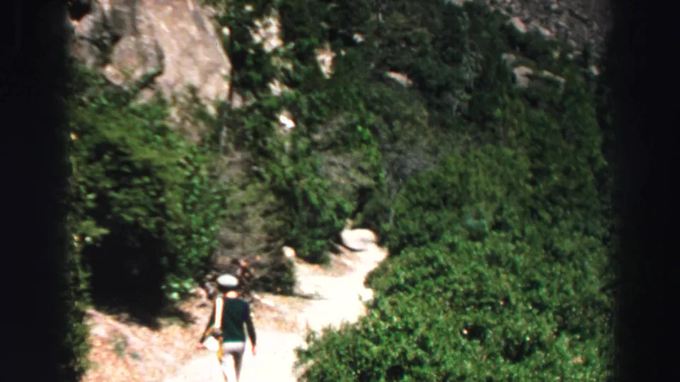 1969 Lake Tahoe-area home-movie frame showing hikers from behind on a rocky, shrub-lined forest trail.