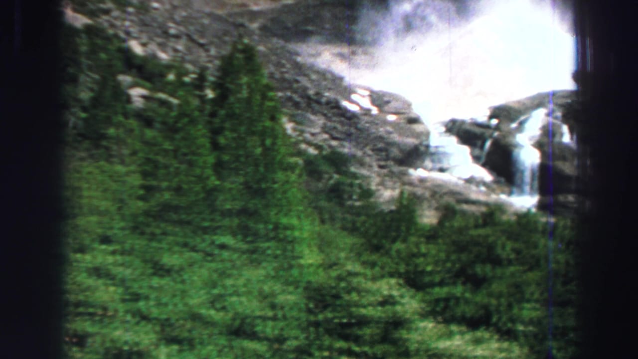 Waterfall rushing through rocks beyond green trees and brush.