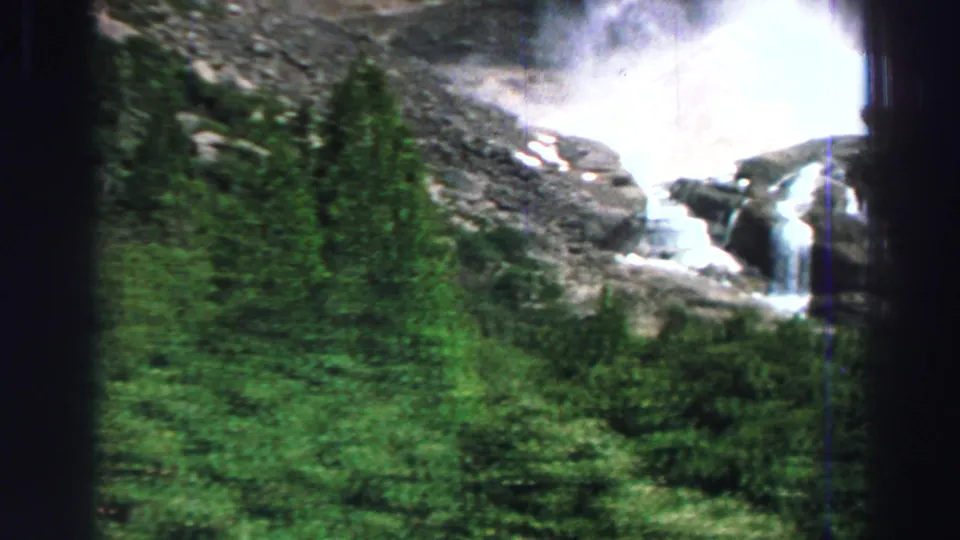 1969 Lake Tahoe frame with a waterfall visible above dense trees and rocky mountain terrain.
