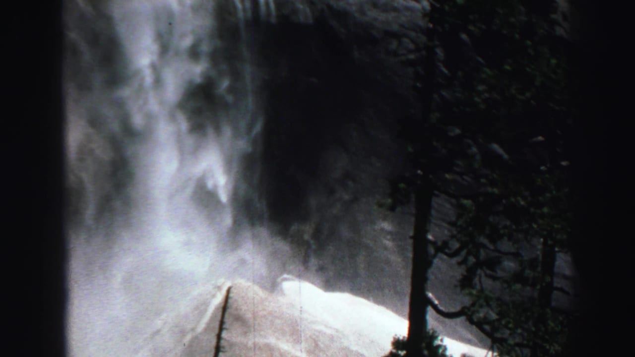 Waterfall spray beside dark trees and rocky cliff edges.