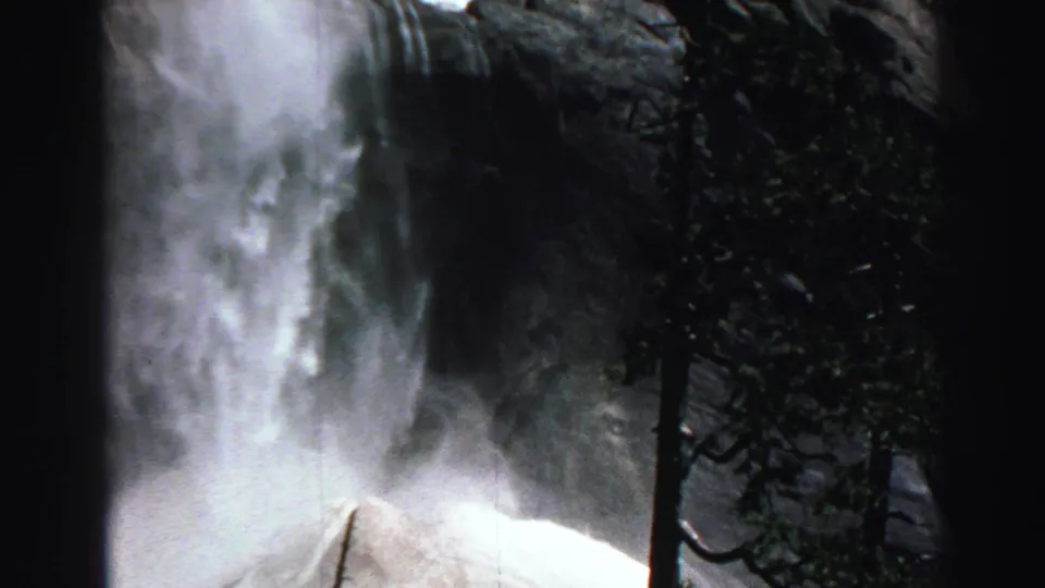 1969 Lake Tahoe 8mm frame with waterfall spray, evergreen branches, and a bright granite cliff surface.