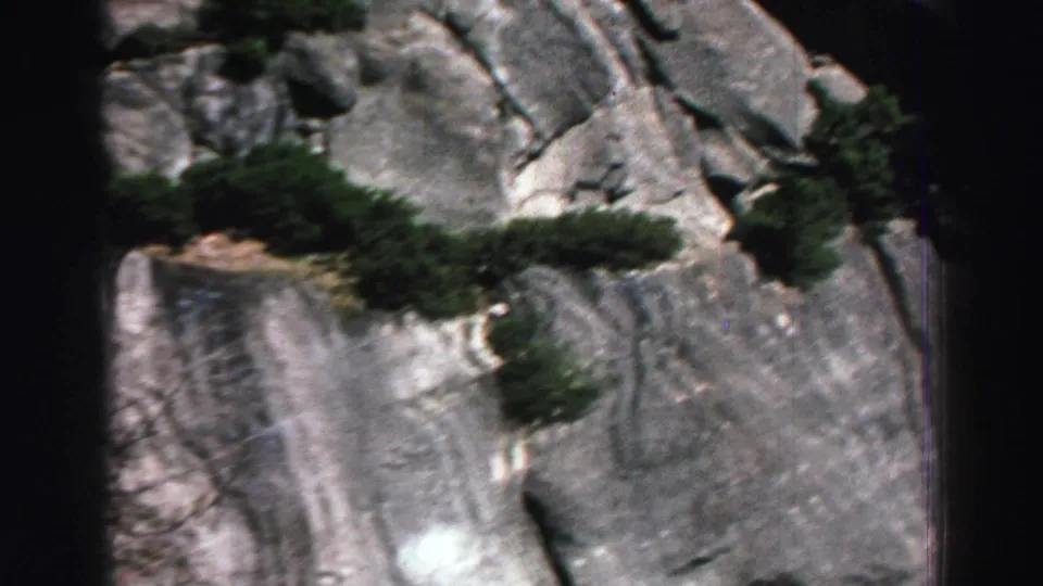 1969 Lake Tahoe 8mm frame showing a pale rock wall, small trees, green shrubs, and dark film-scan borders.