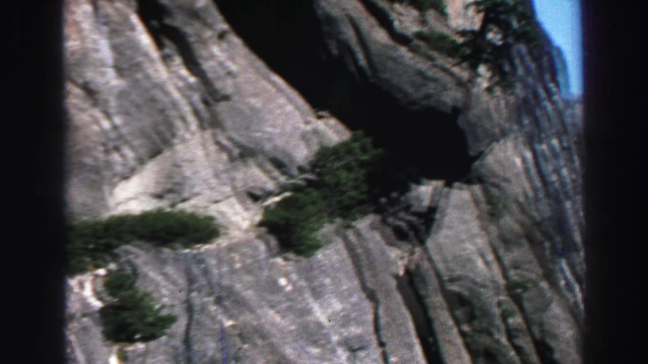 Granite cliff face with shrubs and dark film-frame edges.