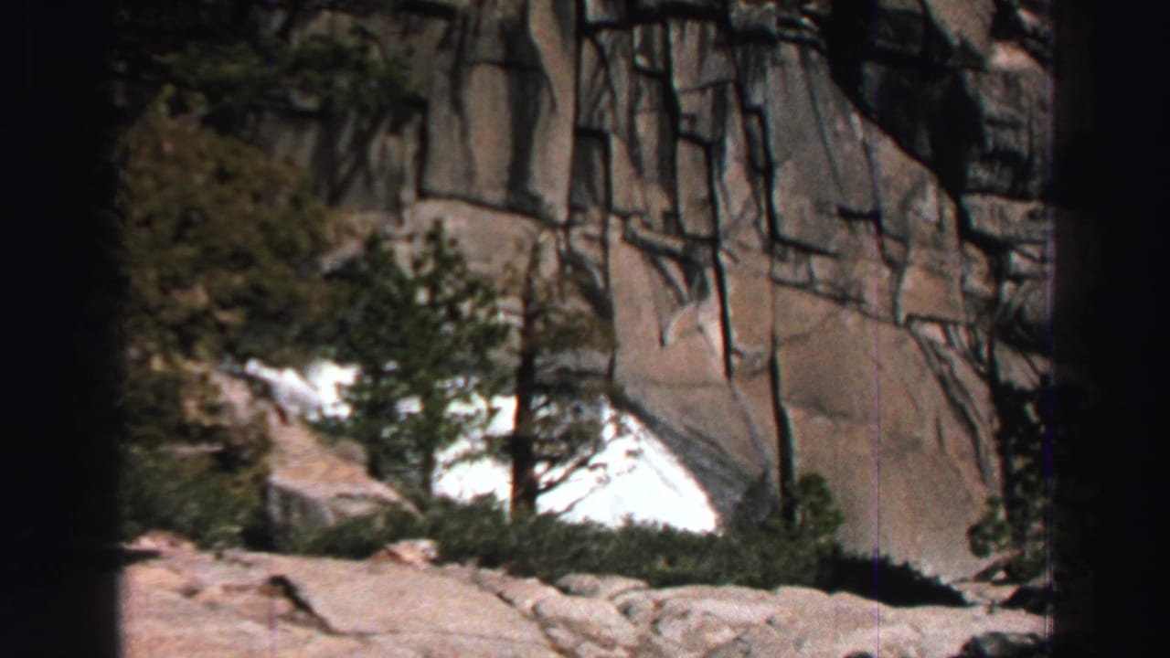 1969 Lake Tahoe 8mm frame with a granite wall, a central evergreen, and bright water or snow near the lower cliff.