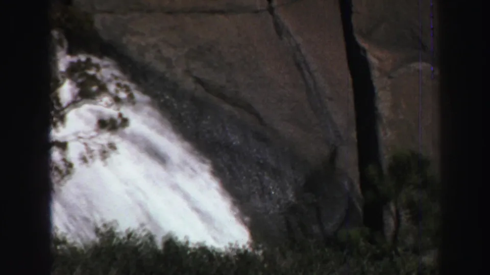 1969 Lake Tahoe 8mm frame showing a close view of white waterfall flow against dark granite and nearby tree cover.