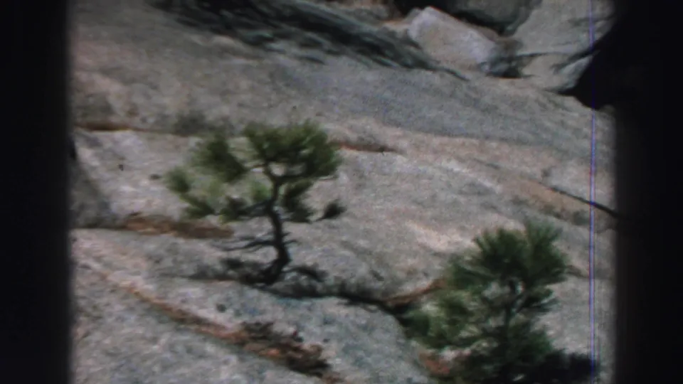 1969 Lake Tahoe 8mm frame of a pale granite hillside with sparse evergreen trees and natural fissures in the stone.