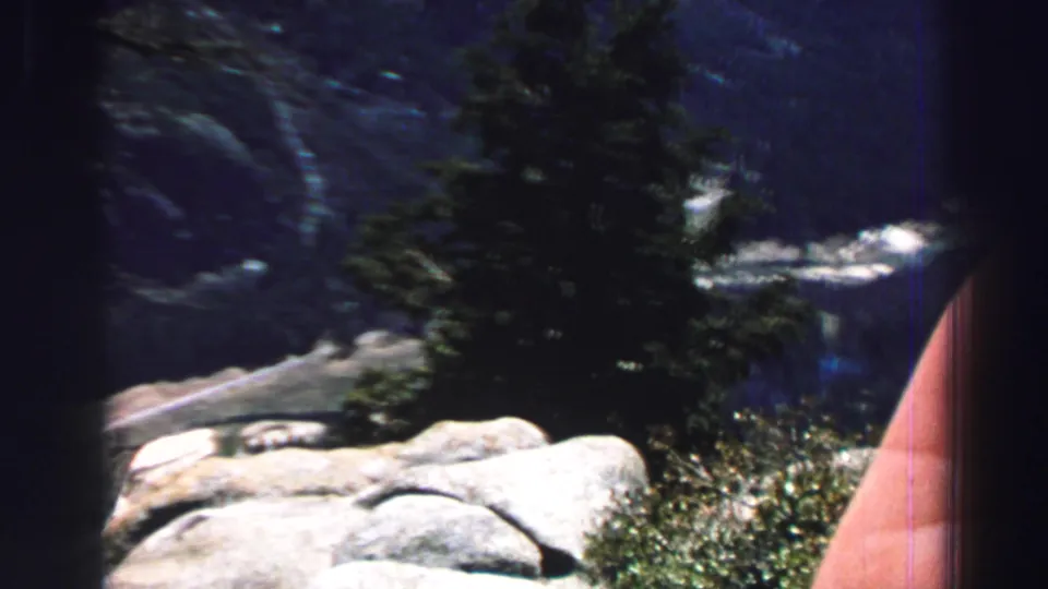 Lake Tahoe 8mm frame with an evergreen, pale rocks, distant blue mountains, and a hand along the right edge.