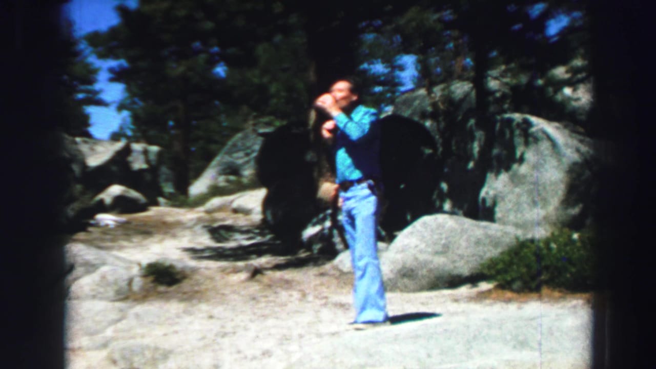 Man in turquoise shirt drinks from a cup on a rocky wooded trail.