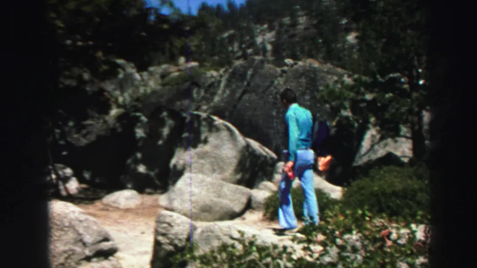 1969 Lake Tahoe frame showing the man from behind as he walks away through rocks and trees after drinking from the cup.