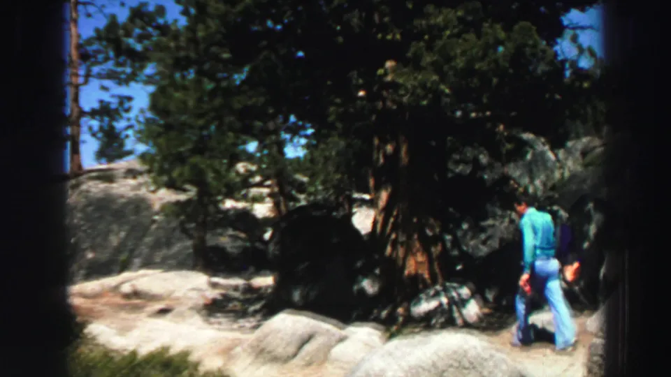 The hiker moves away from the camera through a rocky pine area in the supplied Lake Tahoe, California 1969 footage.