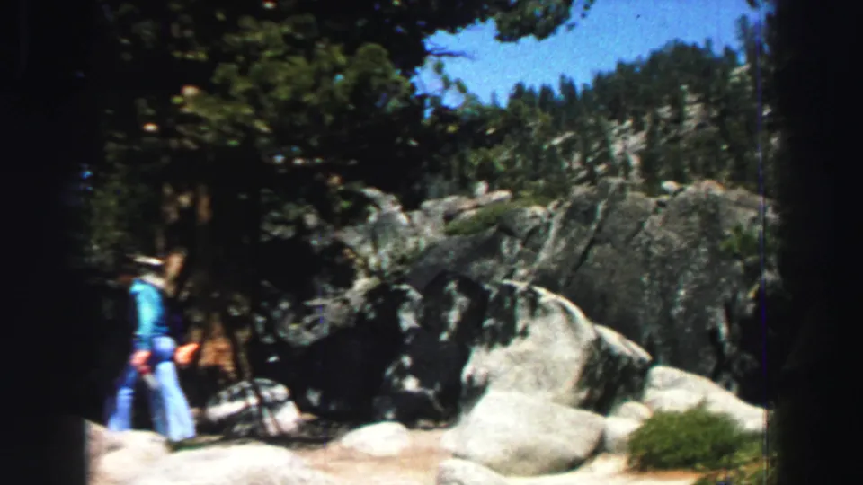 The man in jeans continues along the boulder-lined trail under tall pines in the supplied 1969 Lake Tahoe home-movie footage.