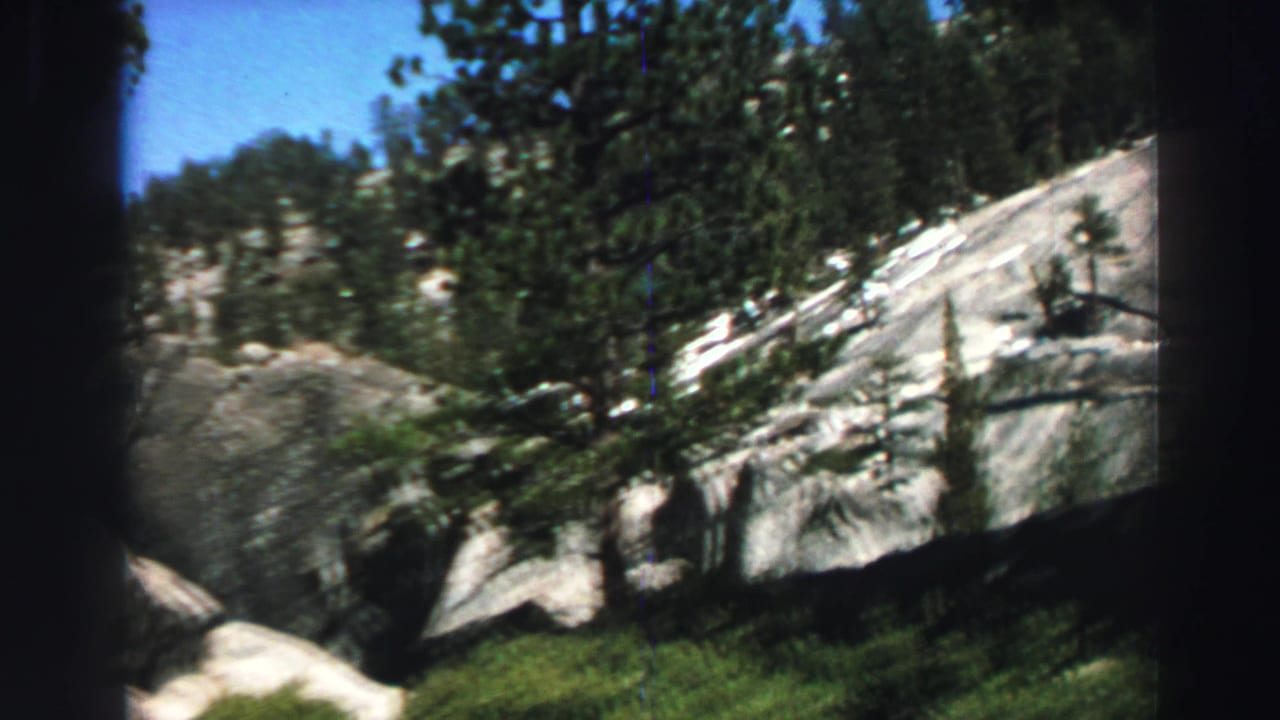 1969 Lake Tahoe frame with evergreen trees against sunlit granite slopes and a clear blue sky.